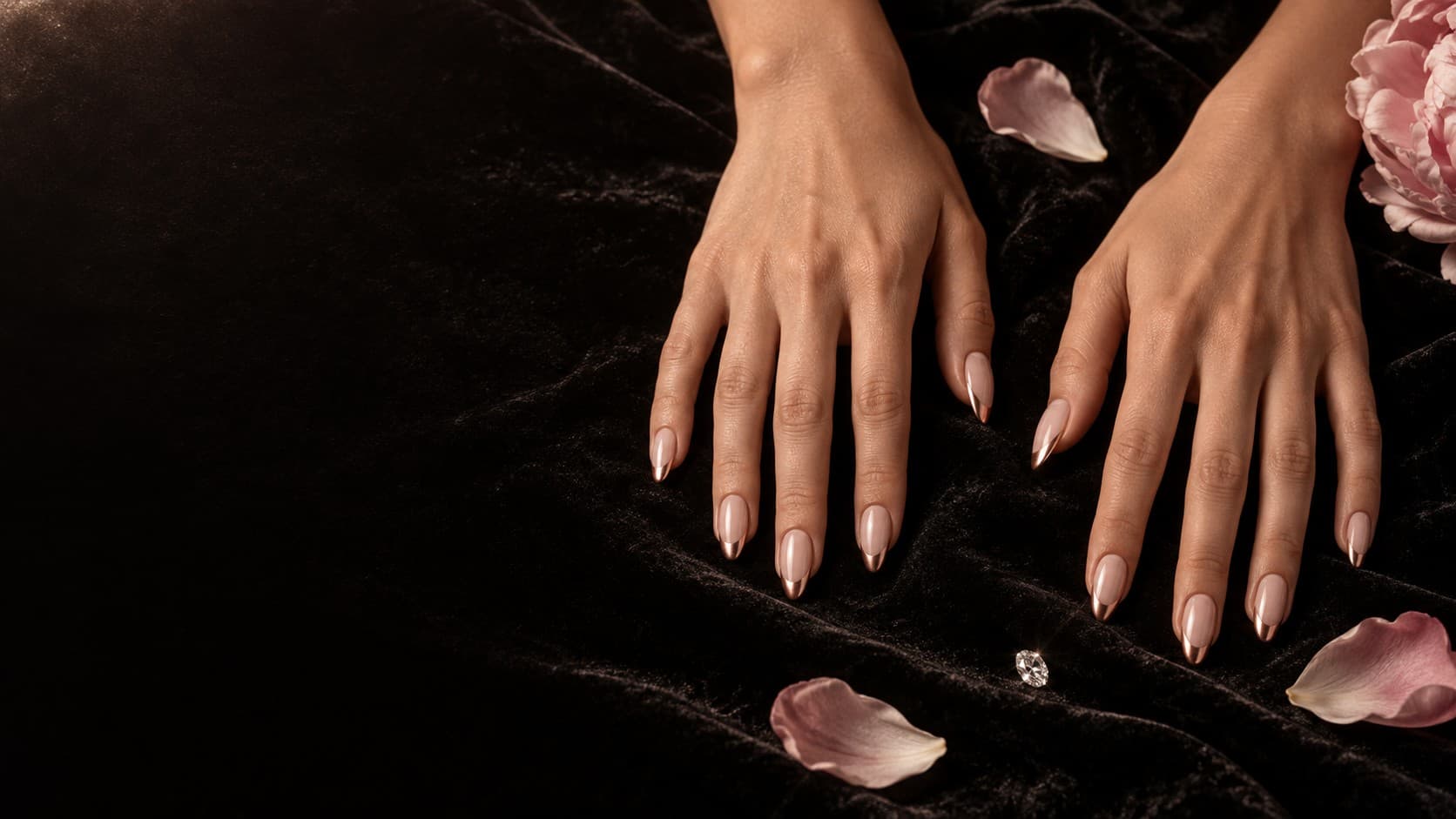 Mains croisées sur velours noir, ongles nude à pointe rose gold, pétales de pivoine